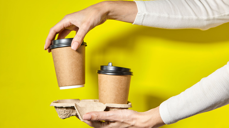 Hands,Holding,Two,Cups,Brown,Paper,With,Black,Lid.,Two
